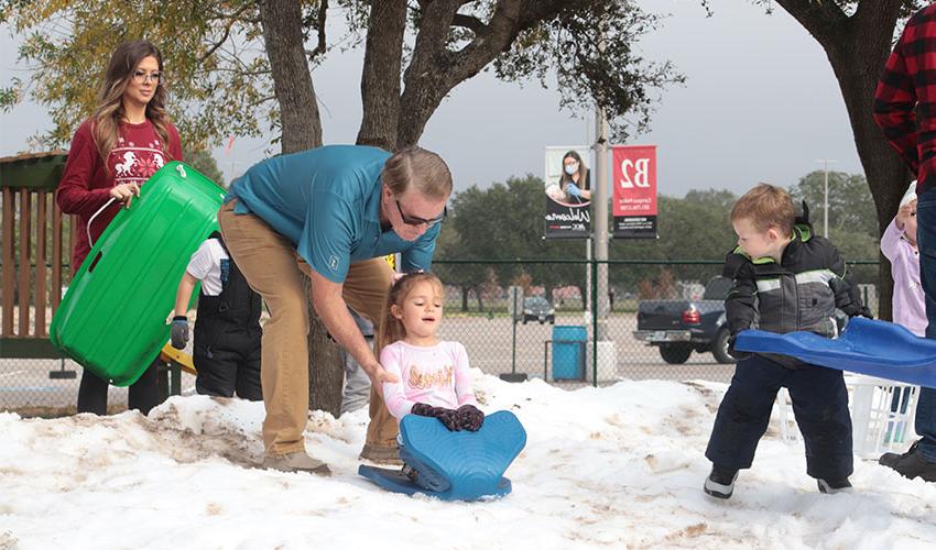 Grandparent  pushing his granddaughter down the snow hill