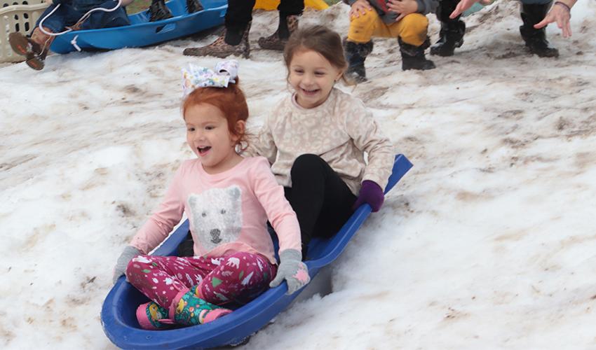 Two girls having fun sliding down the snow hill