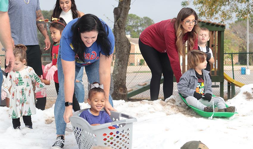 Moms pushing their kids down the snow hill