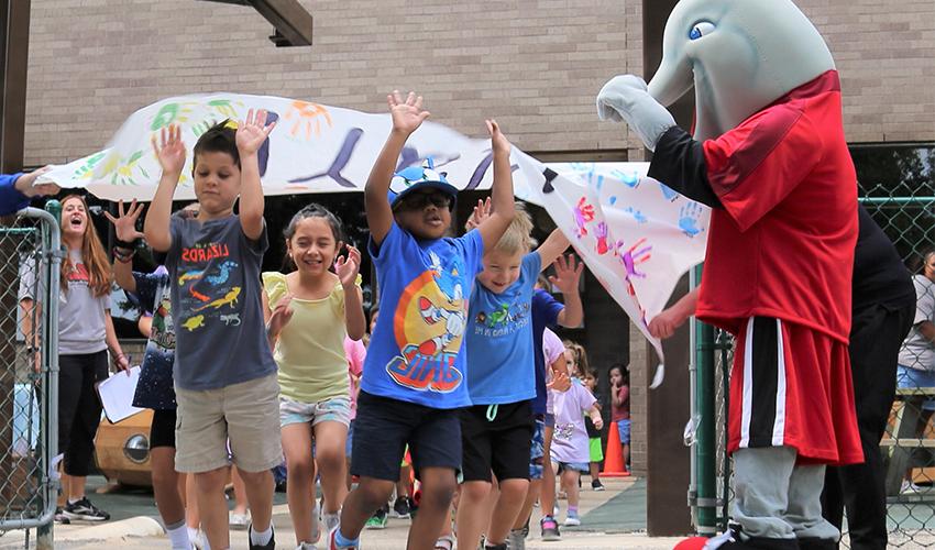 Children run through the Lab School playground reopening banner.