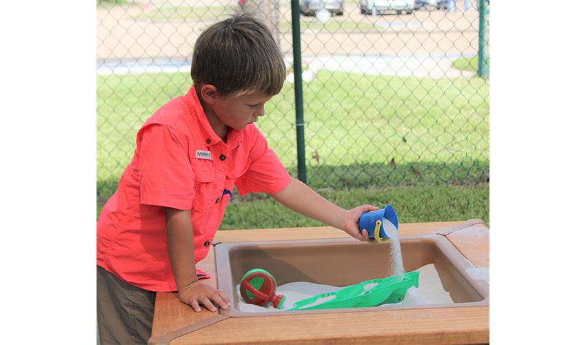 One little boy plays in wooden outdoor sand table.